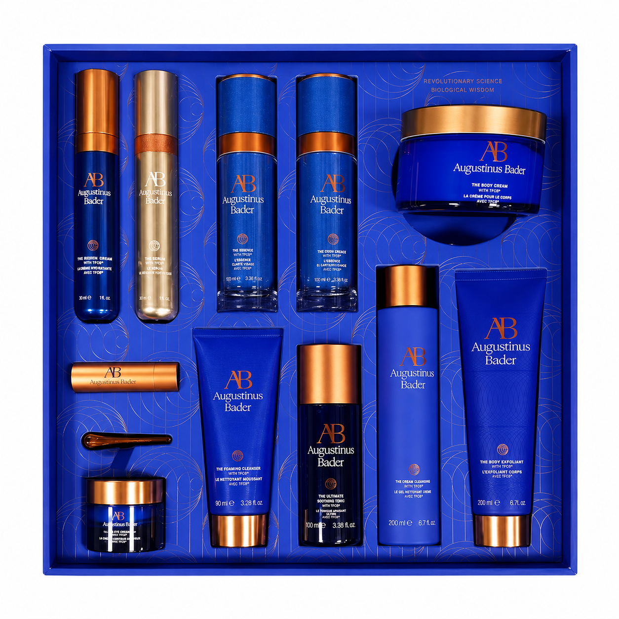 Augustinus Bader skincare gift set in a royal blue box, featuring multiple blue and gold cosmetic bottles, tubes, and jars arranged neatly on a white background.